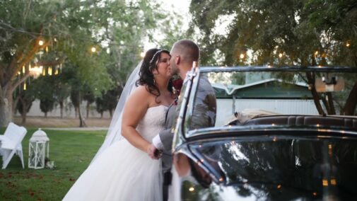 Bride and groom kissing in front of car